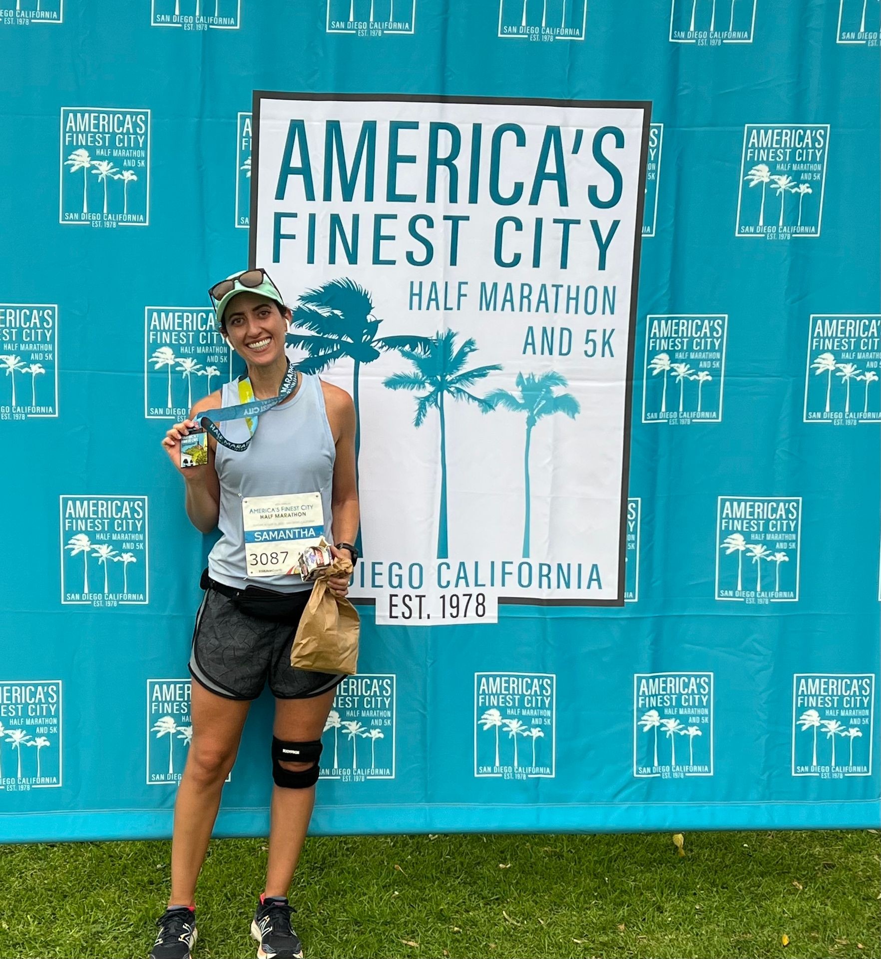 Runner posing with medal in front of America's Finest City Half Marathon banner.