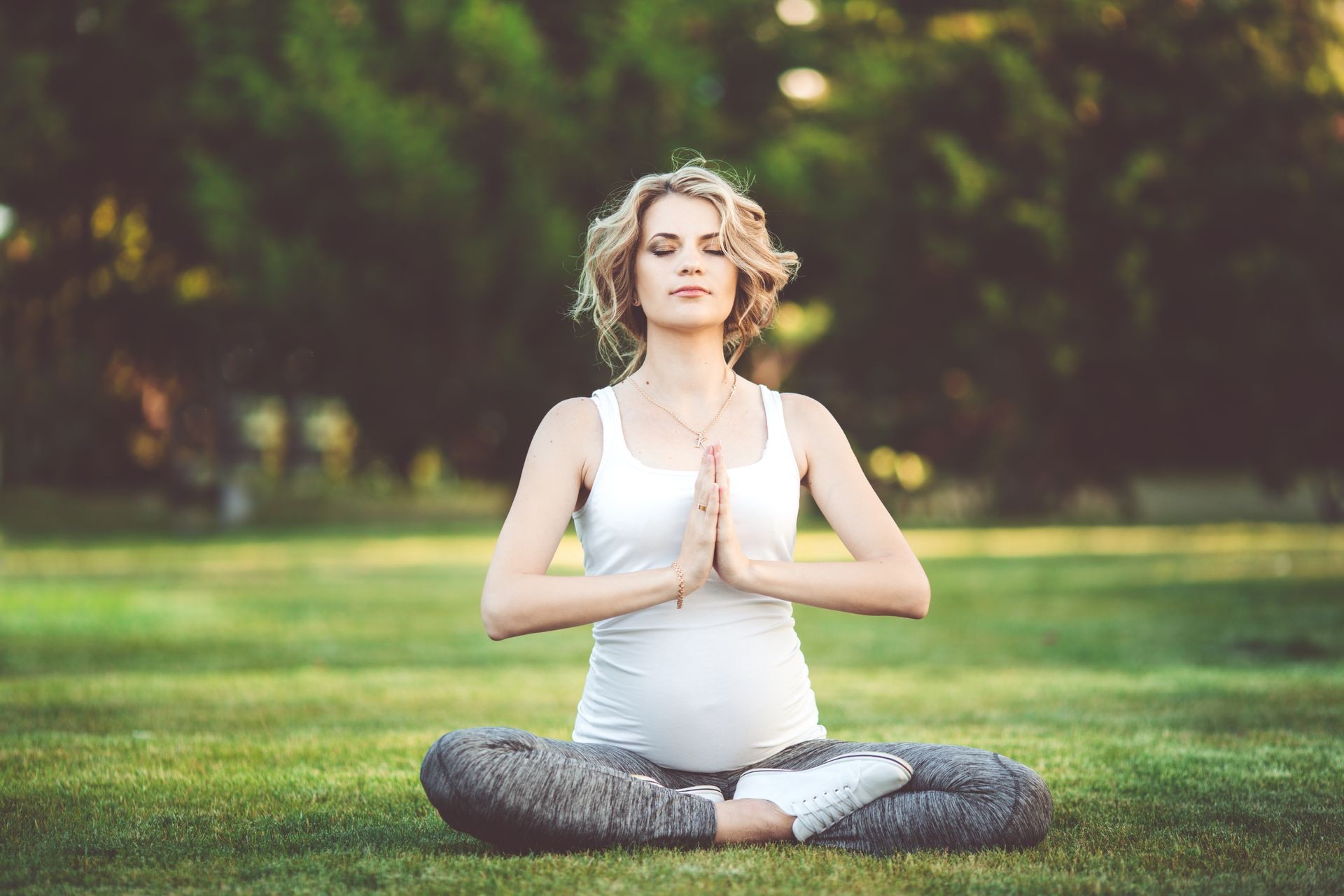 Beautiful slim sportive pregnant girl is doing yoga meditation outdoors